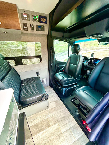 Experience freedom in this spacious RV rental camper van interior. Front seats swivel, lounge area, and control panel visible.