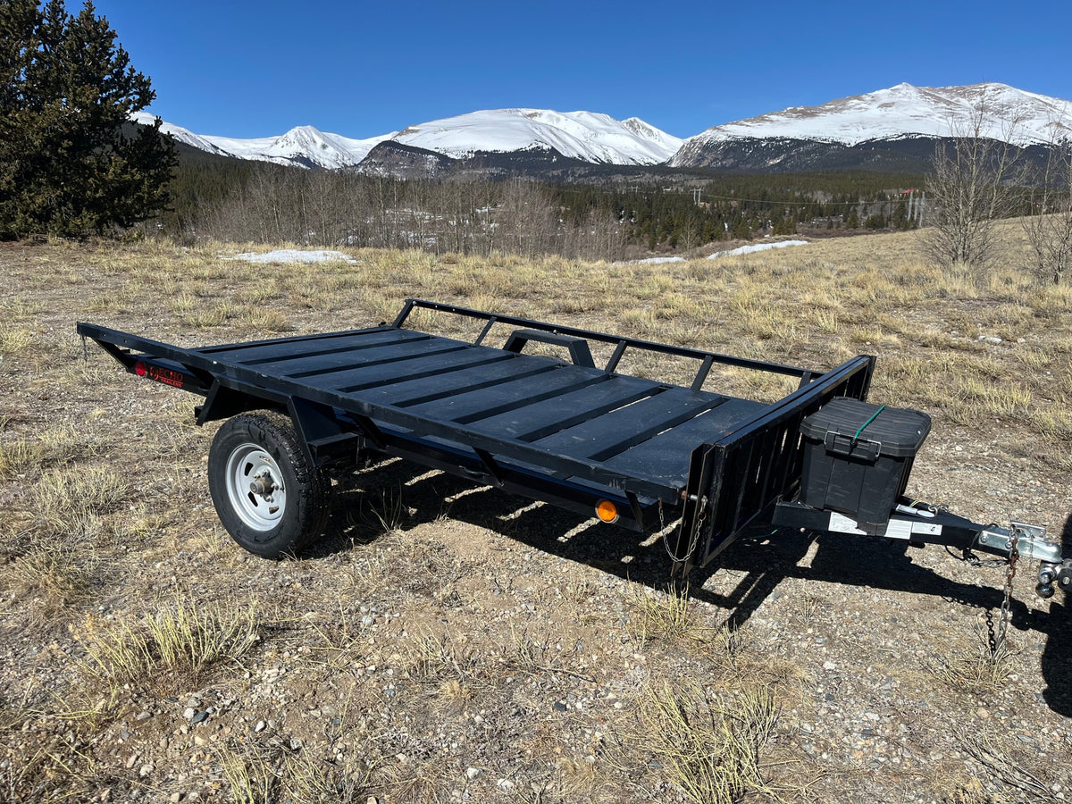 Black utility trailer in scenic mountains. Ideal for outdoor gear on an RV rental adventure.