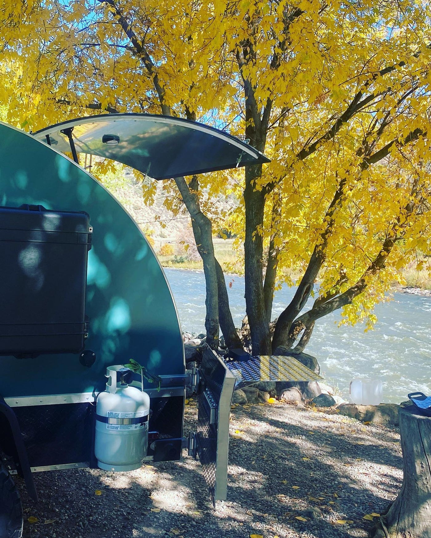 Riverside RV rental adventure with a teardrop camper parked by a vibrant fall tree and flowing river. — photo 4