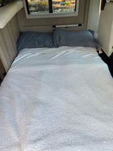 Inside an RV rental, a bed with gray pillows and a white textured blanket offers a cozy sleeping space.