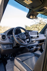 Inside a Mercedes-Benz rv rental van's modern cockpit, featuring the steering wheel, dashboard, gauges, and infotainment screen.