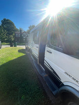 An RV rental camper van, white and black Vista Cruiser, parked in a sunny residential area with its side door open.