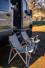 RV rental ready: Storyteller Overland camper van with an attached table and two camping chairs for outdoor relaxation.