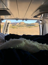 Cozy RV rental bed with open doors revealing a vast desert landscape and mountains. Ideal travel view from inside.