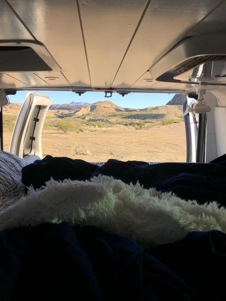 Cozy RV rental bed with open doors revealing a vast desert landscape and mountains. Ideal travel view from inside.