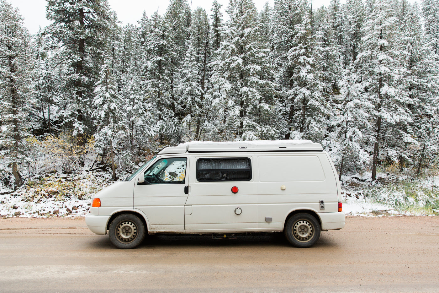 White camper van RV rental parked on a snowy forest road. Ready for your winter adventure.