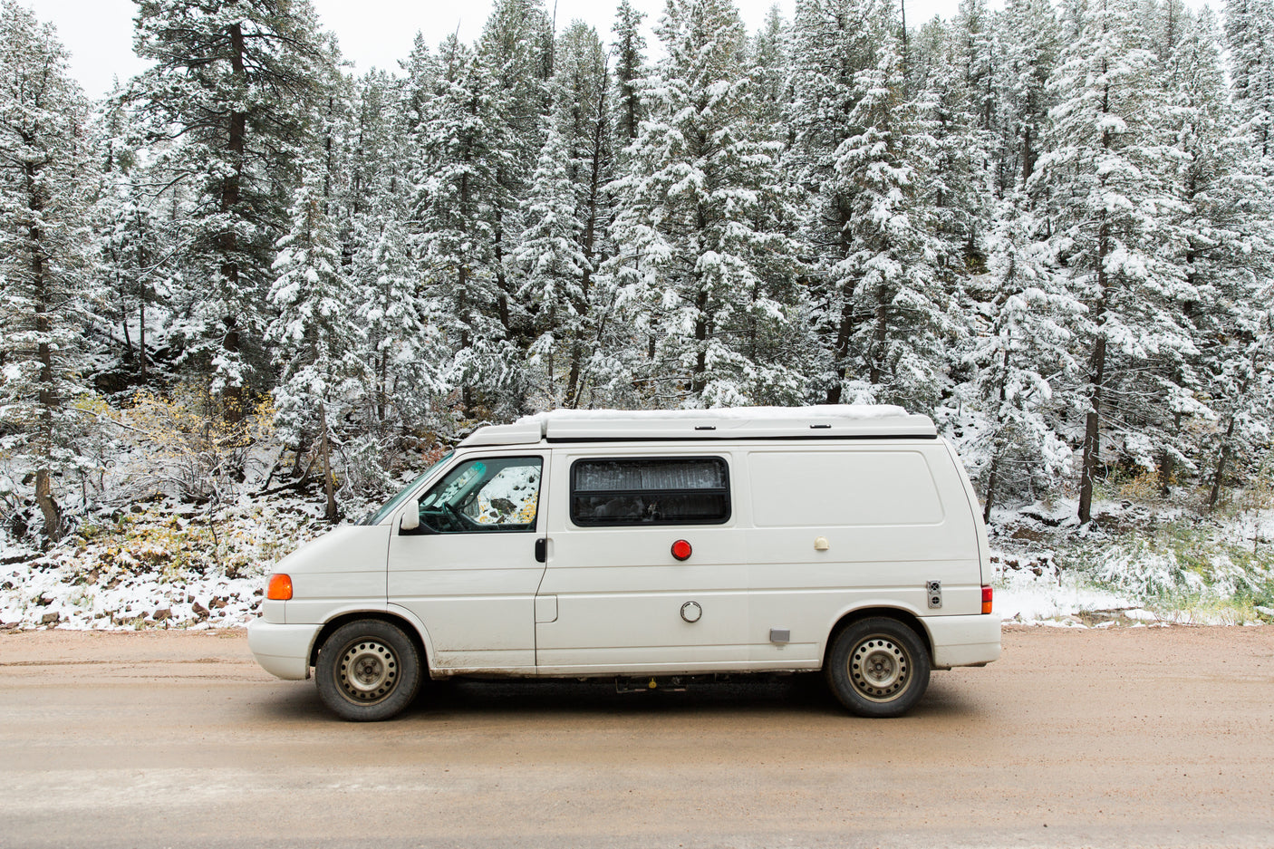 White camper van RV rental parked on a snowy forest road. Ready for your winter adventure.