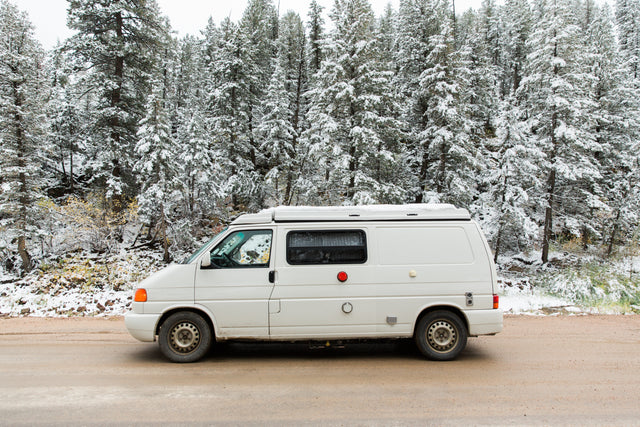 White camper van RV rental parked on a snowy forest road. Ready for your winter adventure.