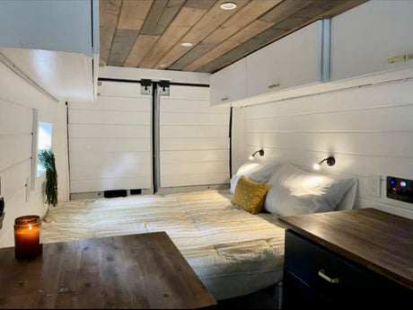 This cozy RV rental features a comfortable van conversion interior with a bed, wooden ceiling, storage cabinets, and a dining table.