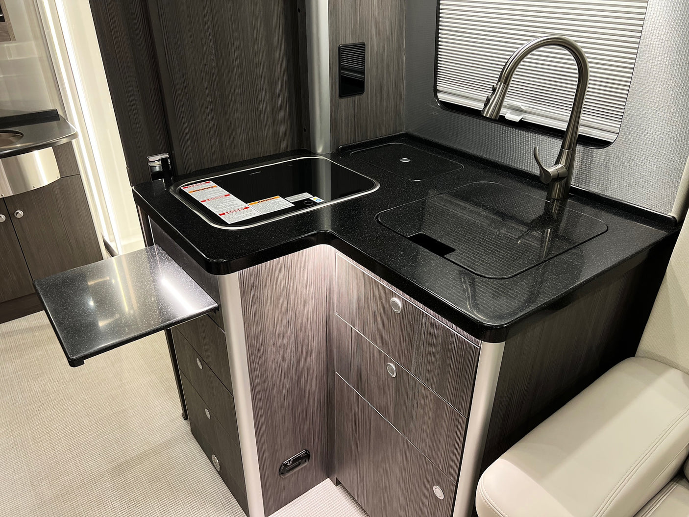 Modern rv rental kitchen with dark cabinets, speckled countertop, sink, induction cooktop, and pull-out extension.