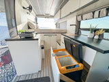 Spacious RV rental interior featuring a modern kitchenette, comfortable bed, and unique pull-out fridge, all with ocean views.