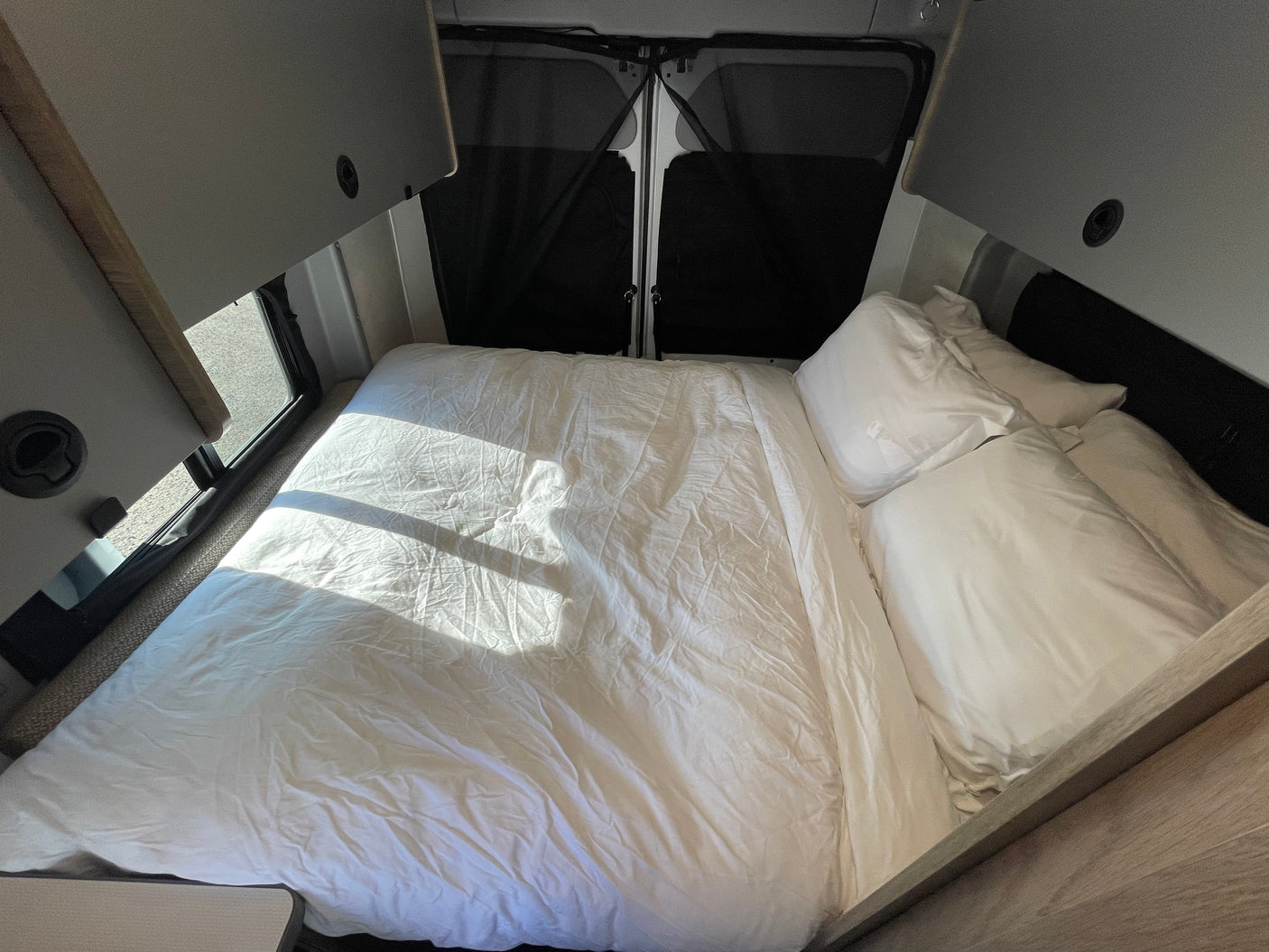 Bright and comfortable RV rental sleeping area with crisp white bedding. Overhead cabinets and rear windows with shades complete this mobile bedroom.
