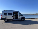 Silver Solis camper van RV rental parked lakeside with doors open, ready for your next adventure.