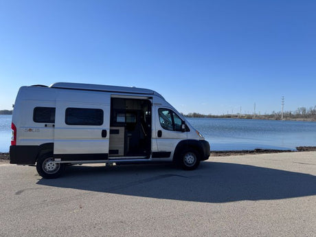 Silver Solis camper van RV rental parked lakeside with doors open, ready for your next adventure.