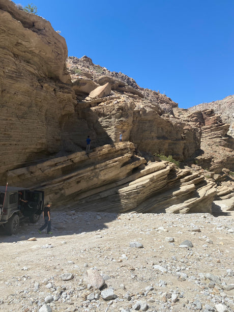 Off-roading in a rugged desert canyon with layered rock walls, a Jeep, and explorers. Imagine this adventure with an RV rental!