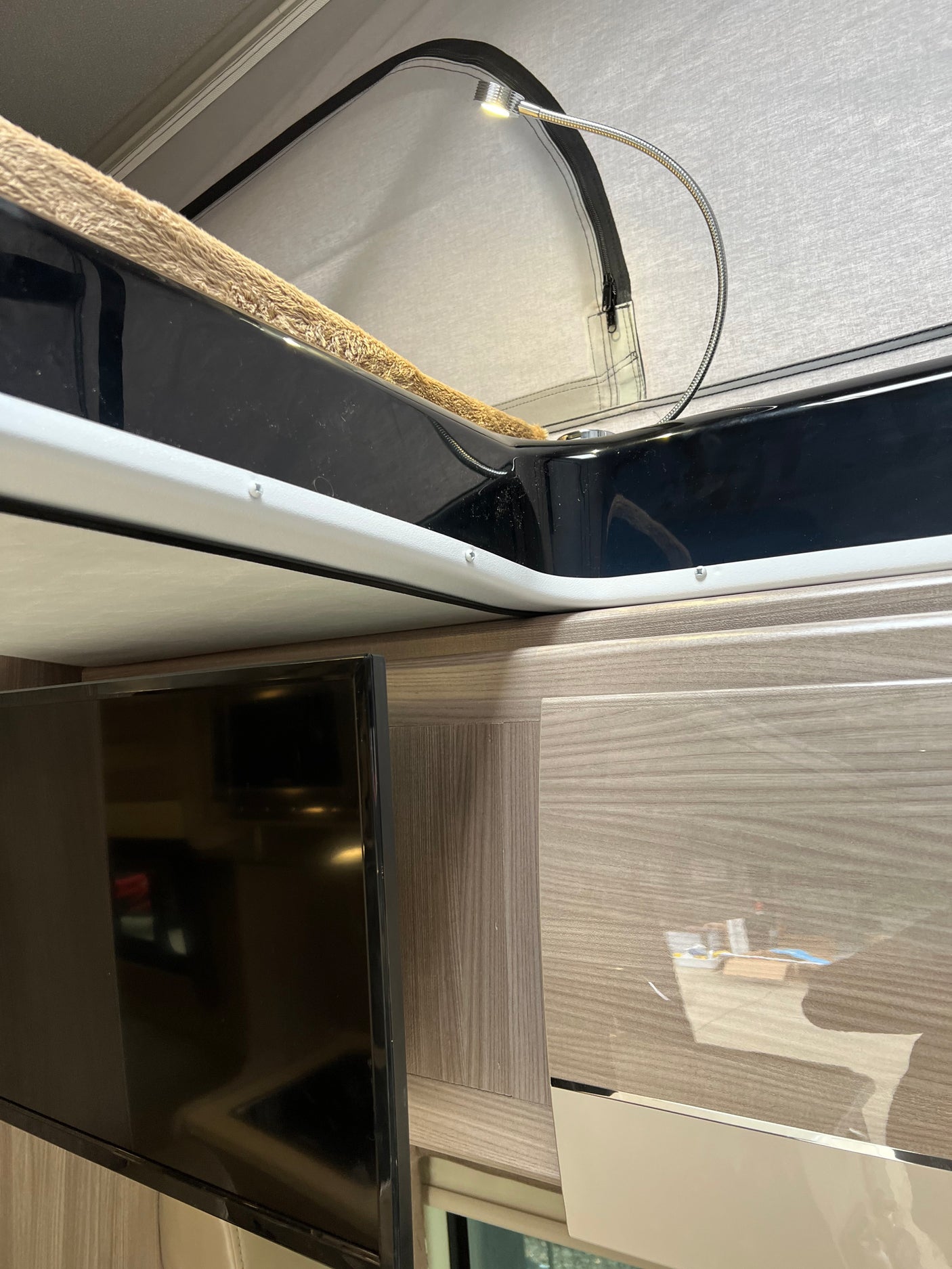 RV rental: View of a compact interior with a bunk bed, reading light, and TV adjacent to wood-grain cabinets.
