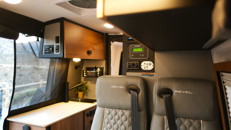 Interior of a Revel rv rental, featuring two padded seats, a detailed control panel, and a compact kitchen counter. Perfect for adventure.