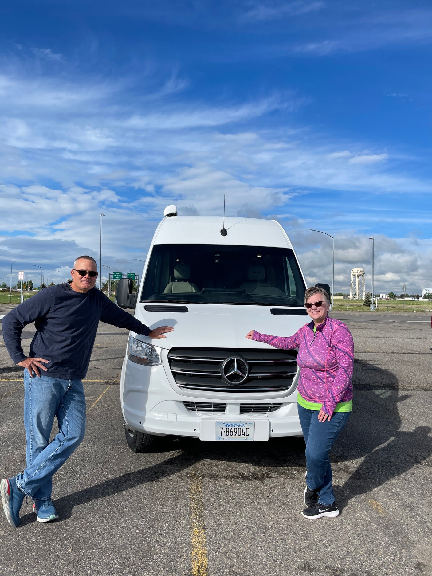 Two people smile proudly with their white Mercedes-Benz Sprinter RV rental, Montana license plate 7-86904C.