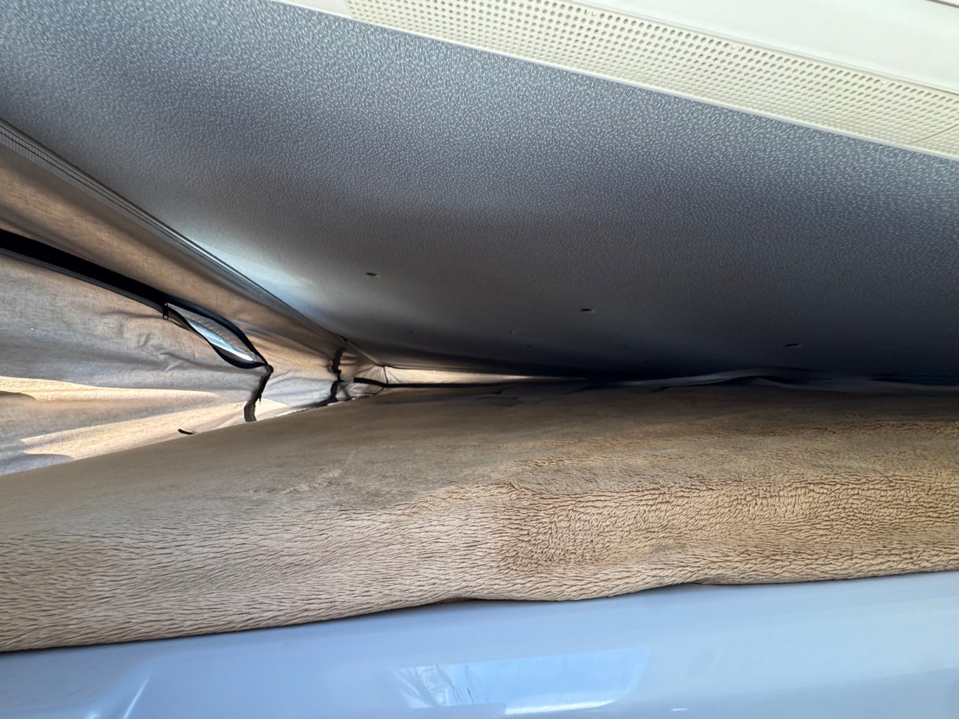 Inside an RV rental pop-top, this view shows the elevated sleeping area with a soft, textured mattress and ventilated ceiling. — photo 12