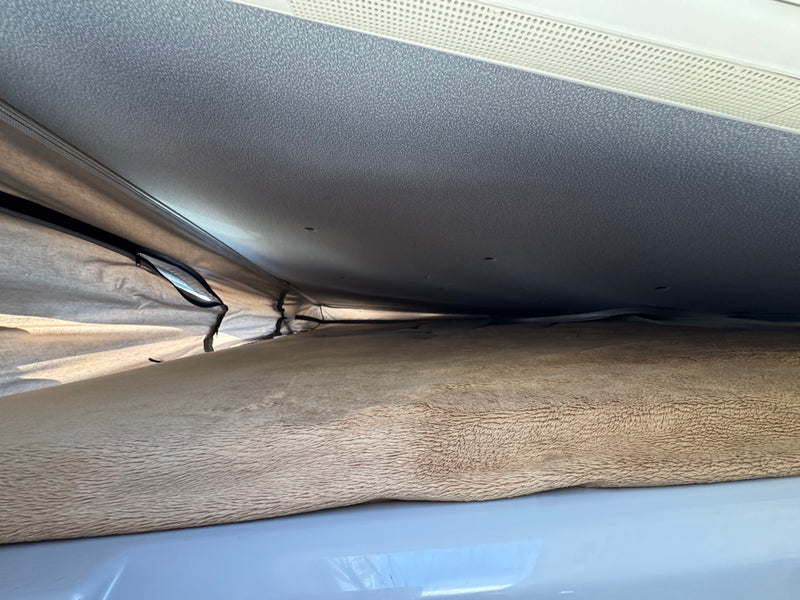 Inside an RV rental pop-top, this view shows the elevated sleeping area with a soft, textured mattress and ventilated ceiling. — photo 12