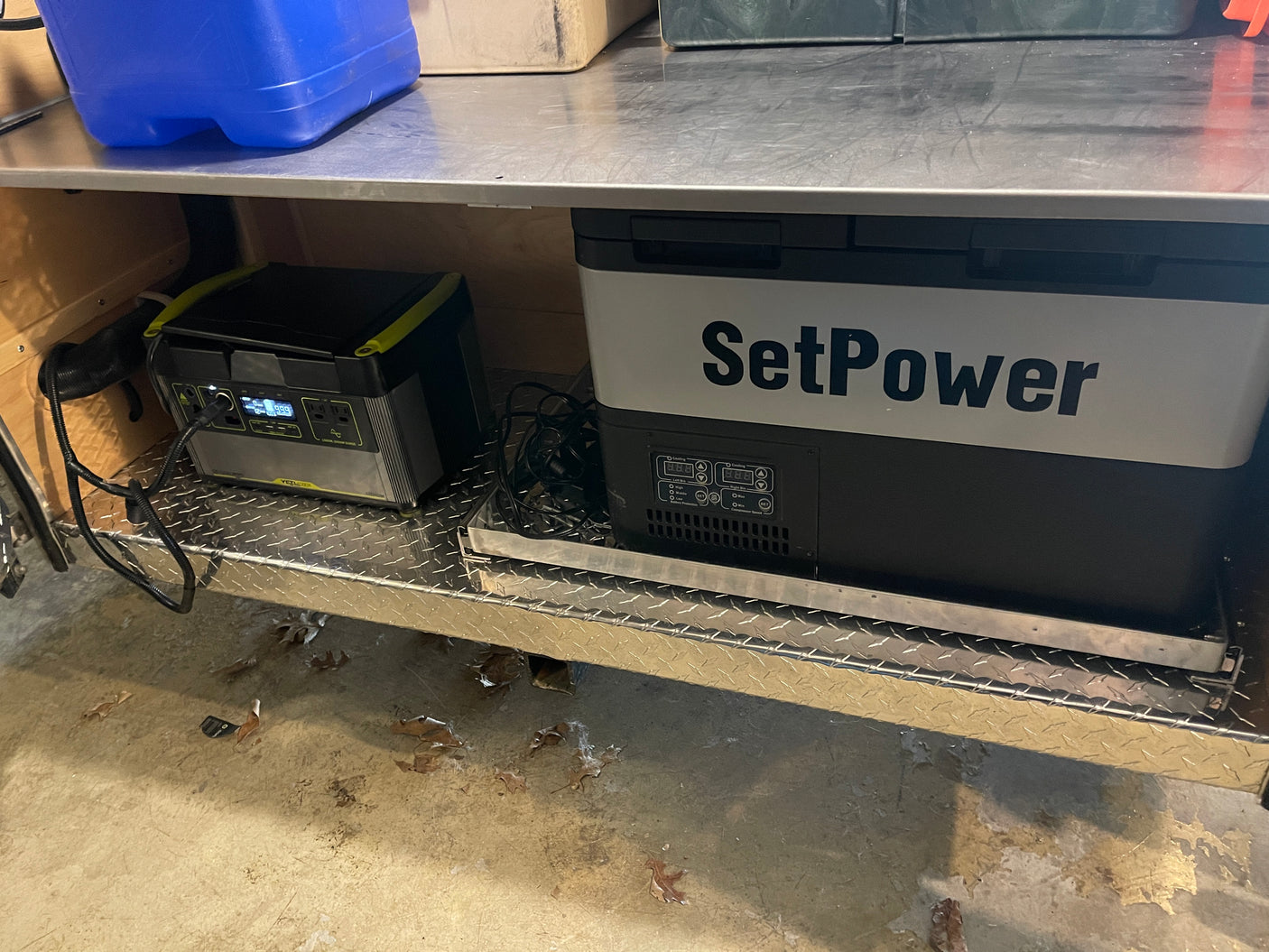This RV rental setup features a portable fridge/freezer and a power station on a diamond plate shelf for off-grid use.