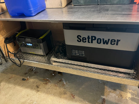 This RV rental setup features a portable fridge/freezer and a power station on a diamond plate shelf for off-grid use.