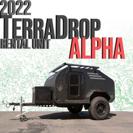 This 2022 TerraDrop Alpha teardrop RV rental unit is a black trailer with off-road tires and a roof rack, parked on asphalt.