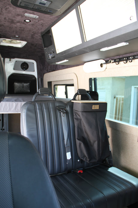 RV rental interior: black leather seats, rear bed, and overhead storage, offering comfort for your travels.