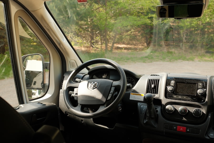  screened window with lush green forest views.|Cozy RV rental bed with striped bedding inside a pop-top camper. Ideal for comfortable rest on your travels.|Compact RV rental interior featuring a kitchen with stovetop — photo 10