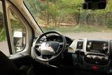 Dashboard and steering wheel of an RV rental, looking out the windshield at a wooded area.