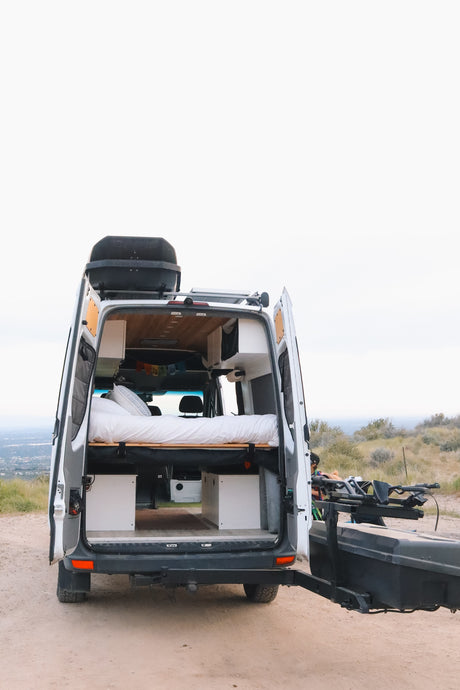 Rear view of a fully equipped camper van rv rental with open doors, revealing a cozy bed & storage. Perfect for a scenic road trip adventure!