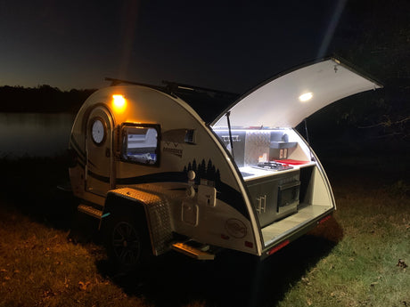Nighttime adventure with an RV rental! This illuminated teardrop camper features a convenient outdoor kitchen, perfect for camping.