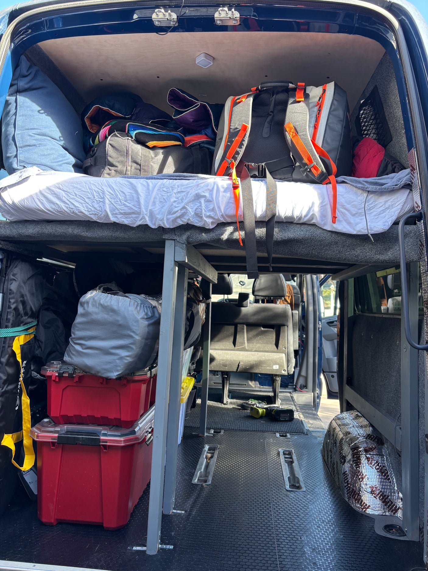 Explore this RV rental's camper van interior, featuring an elevated bed platform, storage bins below, and gear ready for adventure.