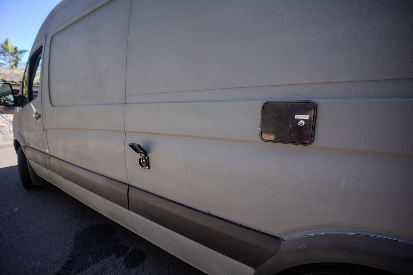 Side view of a light gray RV rental van showing its external water fill port and electrical hookup. — photo 15