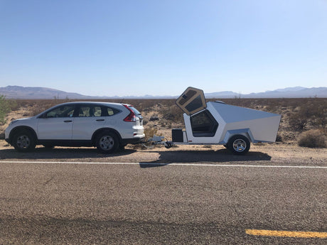 White SUV towing an angular, modern camper trailer. Parked roadside in a vast desert; consider this RV rental for trips.