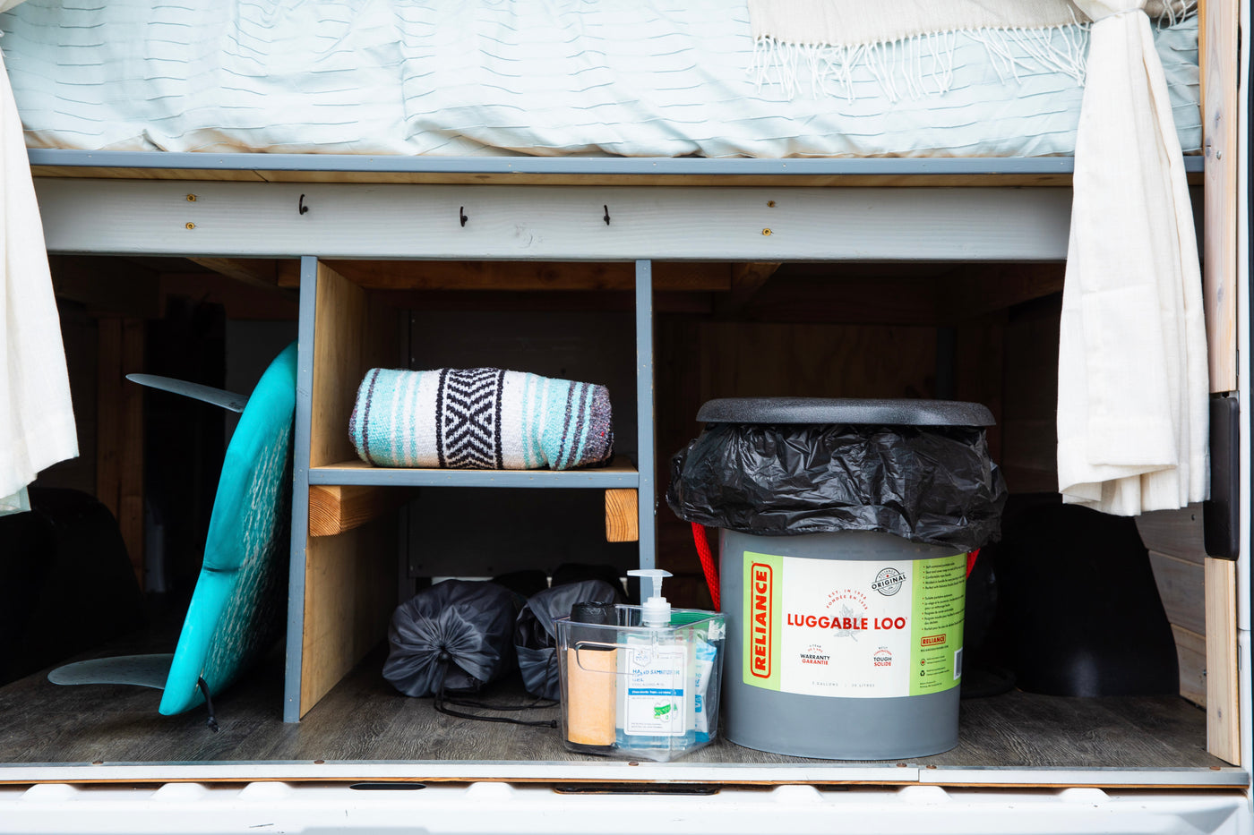 Organized storage in an RV rental, featuring a surfboard, blanket, portable toilet, and hand sanitizer for on-the-go convenience. — photo 17
