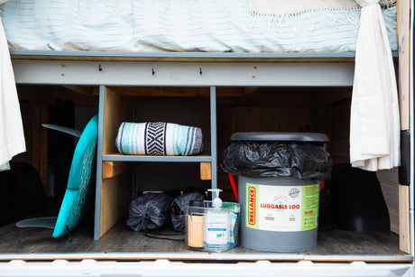 Organized storage in an RV rental, featuring a surfboard, blanket, portable toilet, and hand sanitizer for on-the-go convenience.