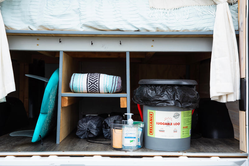 Organized storage in an RV rental, featuring a surfboard, blanket, portable toilet, and hand sanitizer for on-the-go convenience. — photo 17