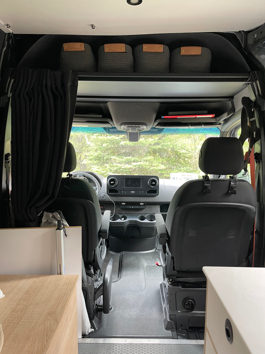 Interior of an rv rental camper van, showcasing the front cab, dashboard, seats, and overhead storage bins.