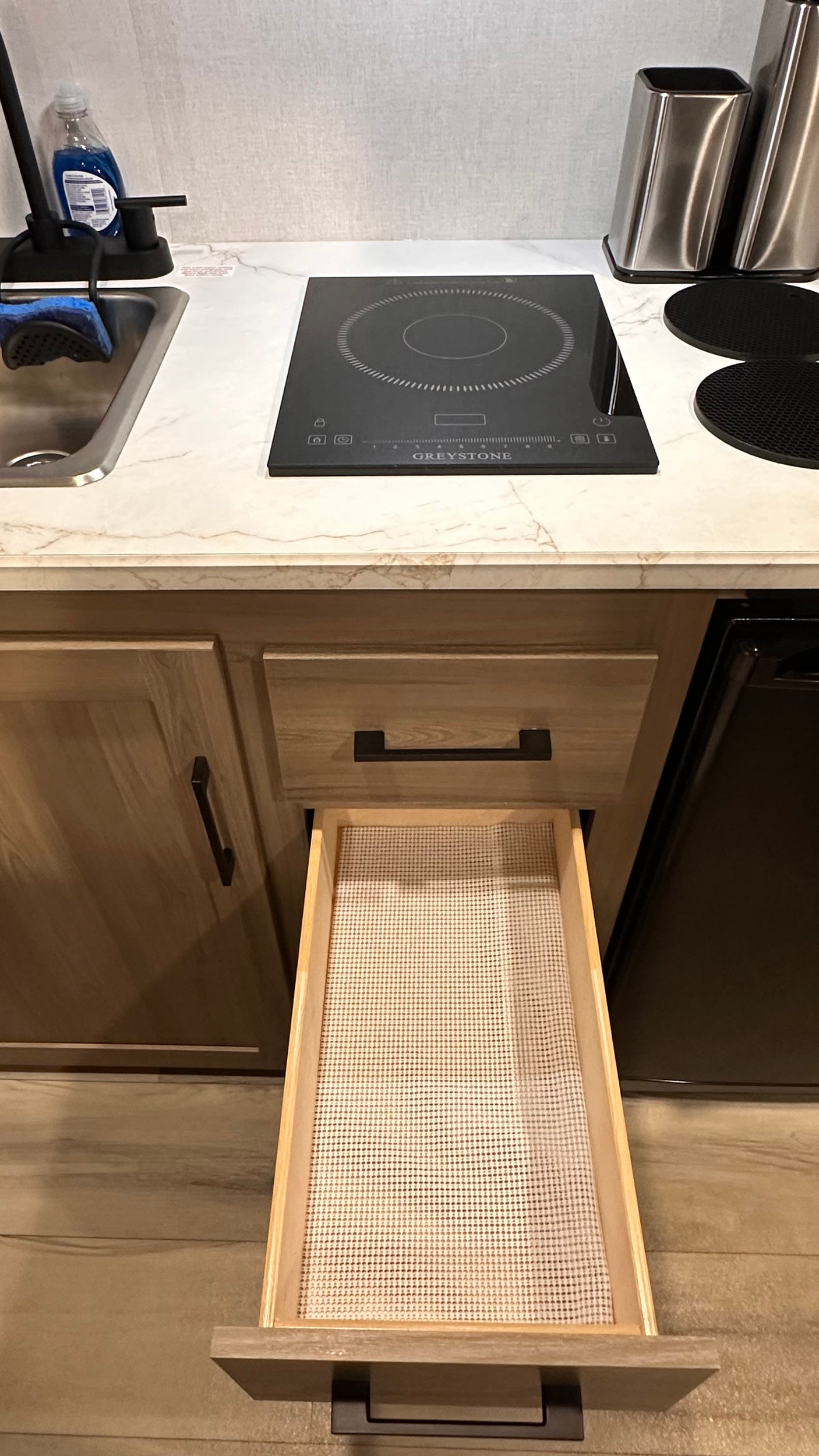 RV rental: Modern kitchen with induction cooktop, sink, wood cabinets, and open drawer with a liner.