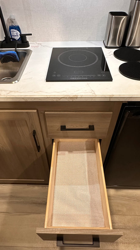 RV rental: Modern kitchen with induction cooktop, sink, wood cabinets, and open drawer with a liner.