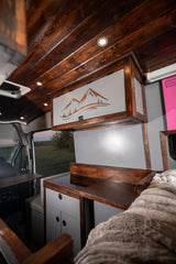 Cozy custom camper van interior, ready for your next adventure. Perfect for an rv rental, featuring wood and mountain art.