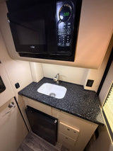 Compact RV rental kitchen: High Pointe microwave (0:00), sink, dark counter, and small fridge for convenient on-the-road cooking.