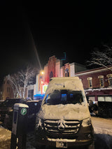 A snow-covered Mercedes-Benz rv rental on a winter night street. Bright theater marquee & icicles adorn background buildings.