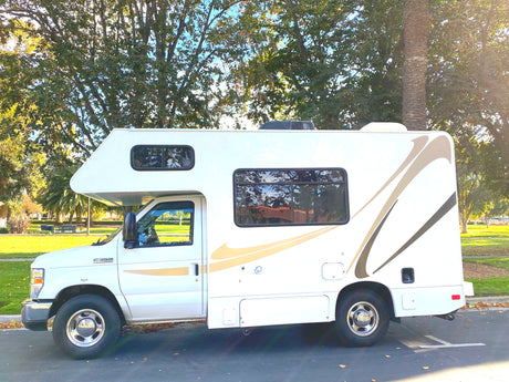 This white Class C RV rental, a Ford E-350, is parked in a sunny park, ready for your next adventure.