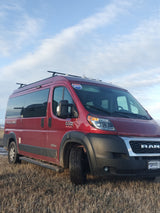 A red Pleasure-Way Tofino RAM Promaster camper van, ideal for RV rental, is parked in a golden field under a blue sky.