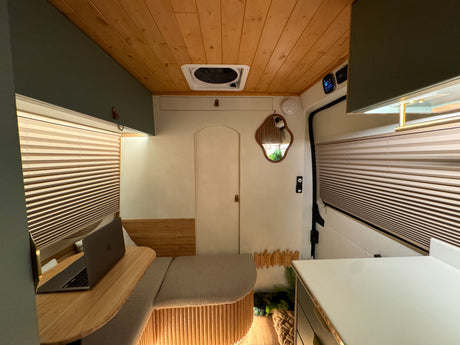 Cozy camper van RV rental interior featuring a bright living space, wooden ceiling, and a comfortable desk setup.