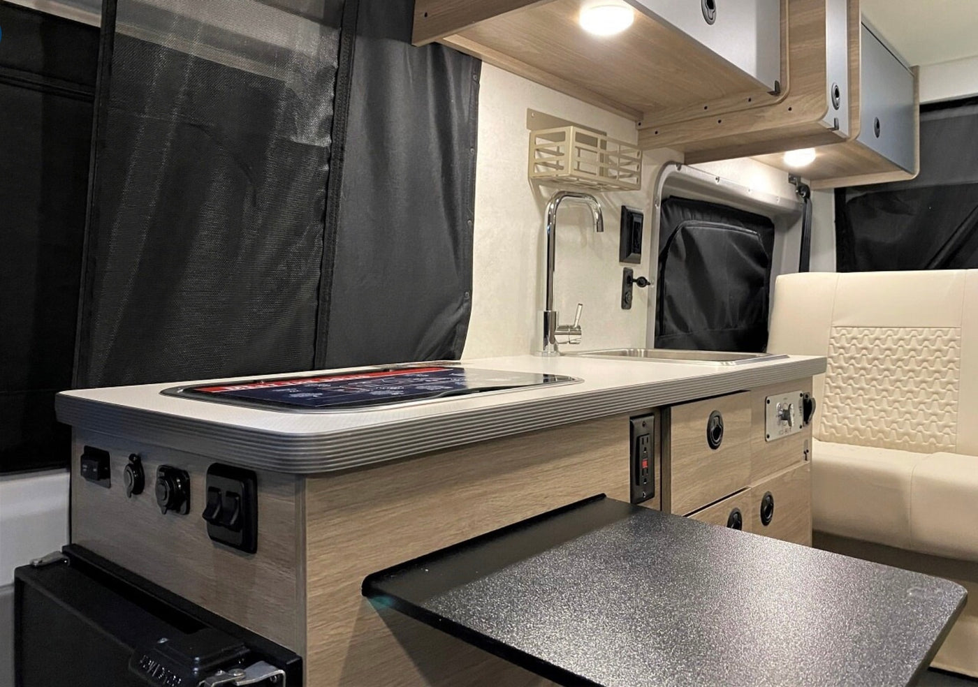 Inside an RV rental, a compact galley features a stainless steel sink, induction cooktop, and light wood cabinetry with pull-out table. — photo 4
