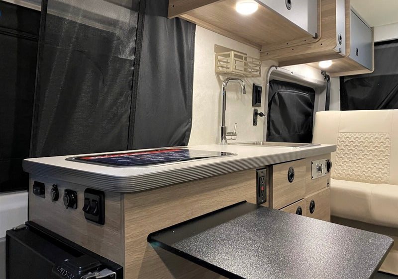 Inside an RV rental, a compact galley features a stainless steel sink, induction cooktop, and light wood cabinetry with pull-out table. — photo 4