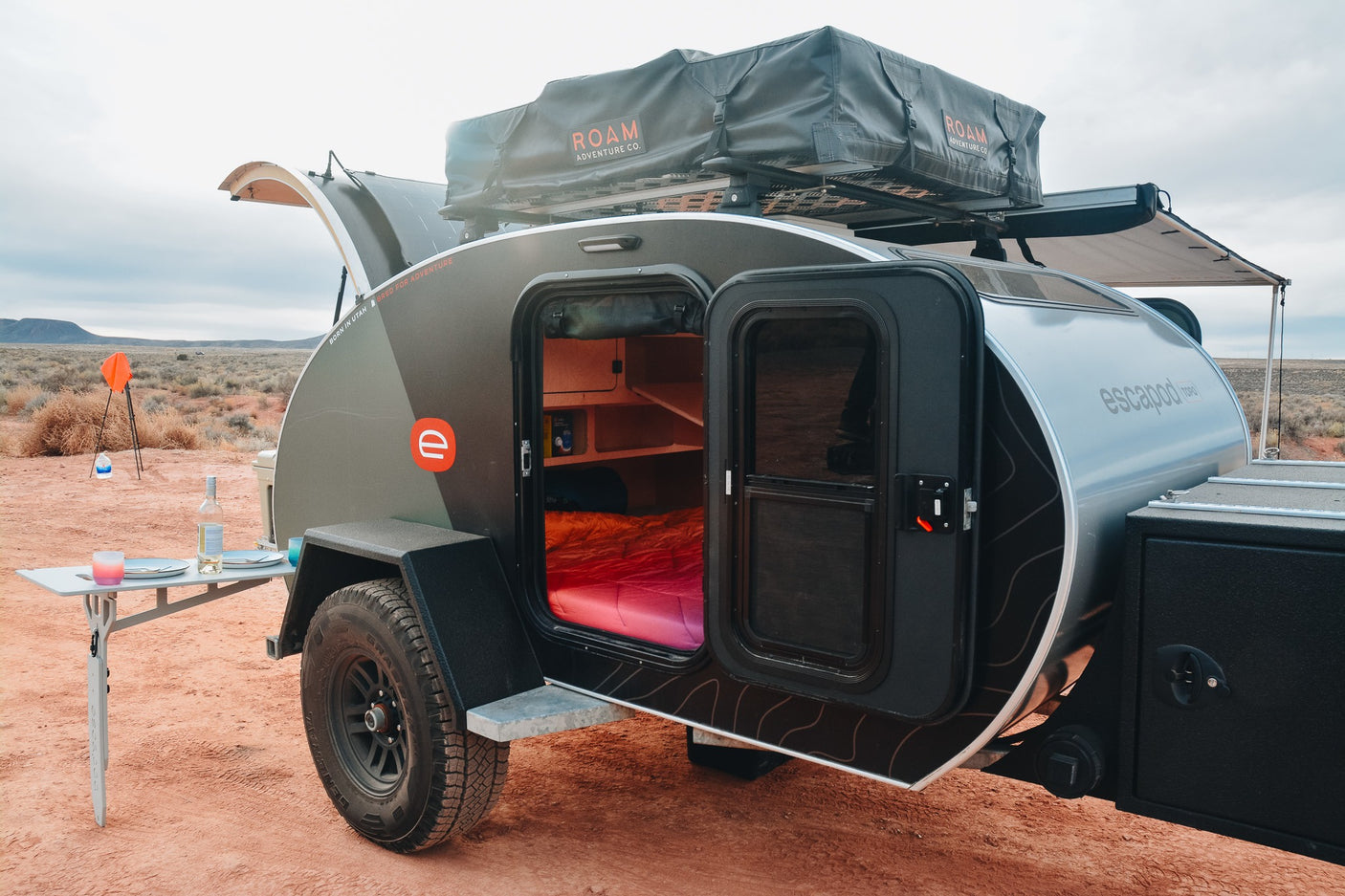 This Escapade teardrop camper, an ideal RV rental, offers adventure with its rooftop tent & outdoor setup in the desert.